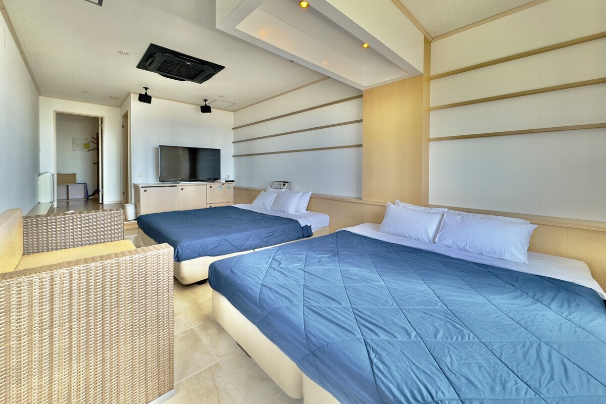 A hotel room with two beds, a television, and a kitchenette.