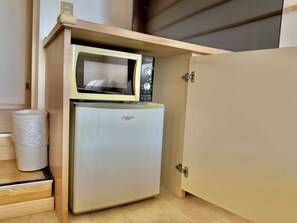 A compact kitchenette with a microwave and refrigerator, a trash bin, and a wooden cabinet. - HOTEL PACIFIC VIEW (Okinawa)