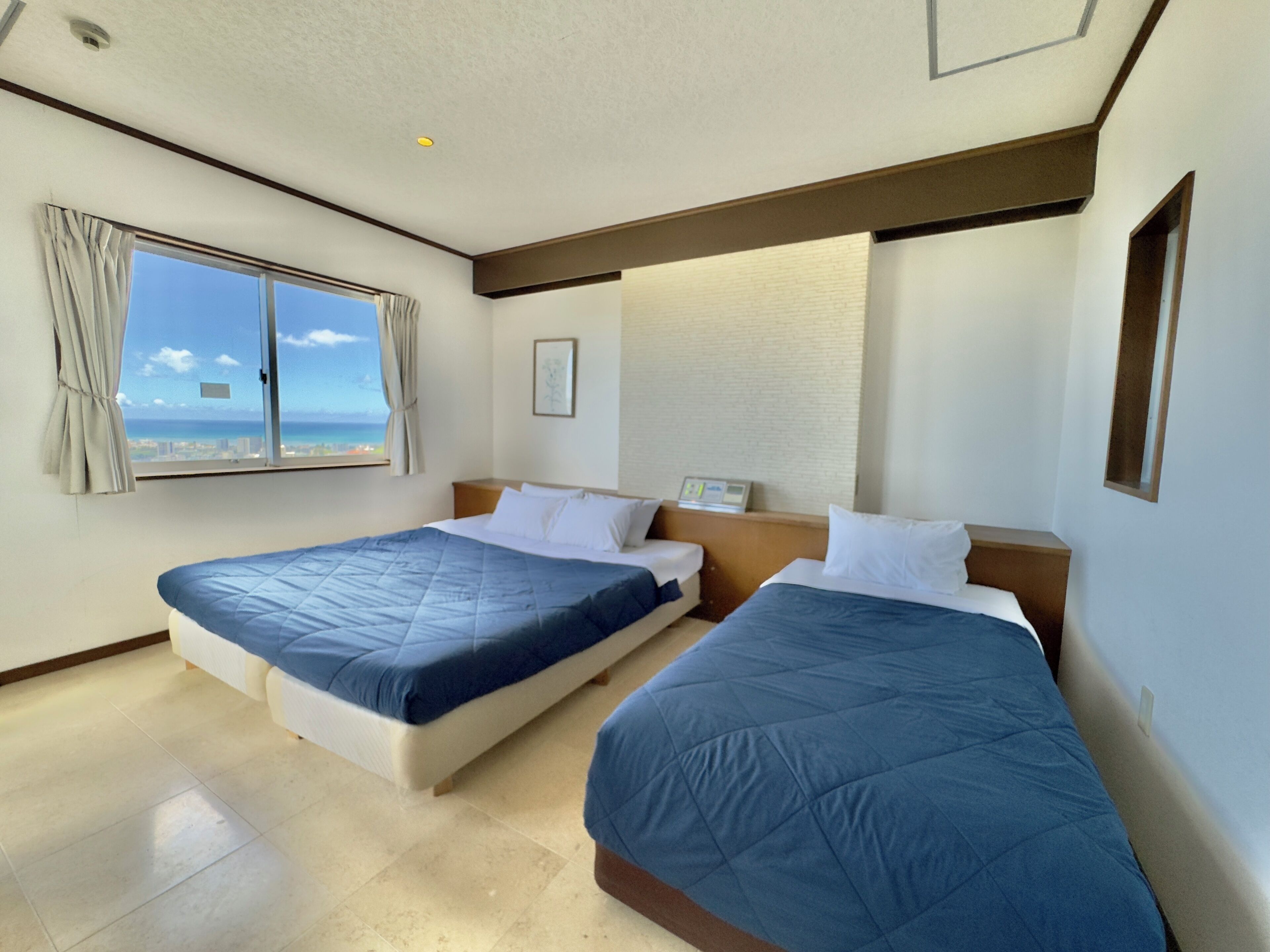 Une chambre d’hôtel avec deux lits, une fenêtre avec des rideaux, une vue sur l’océan et un luminaire au plafond.