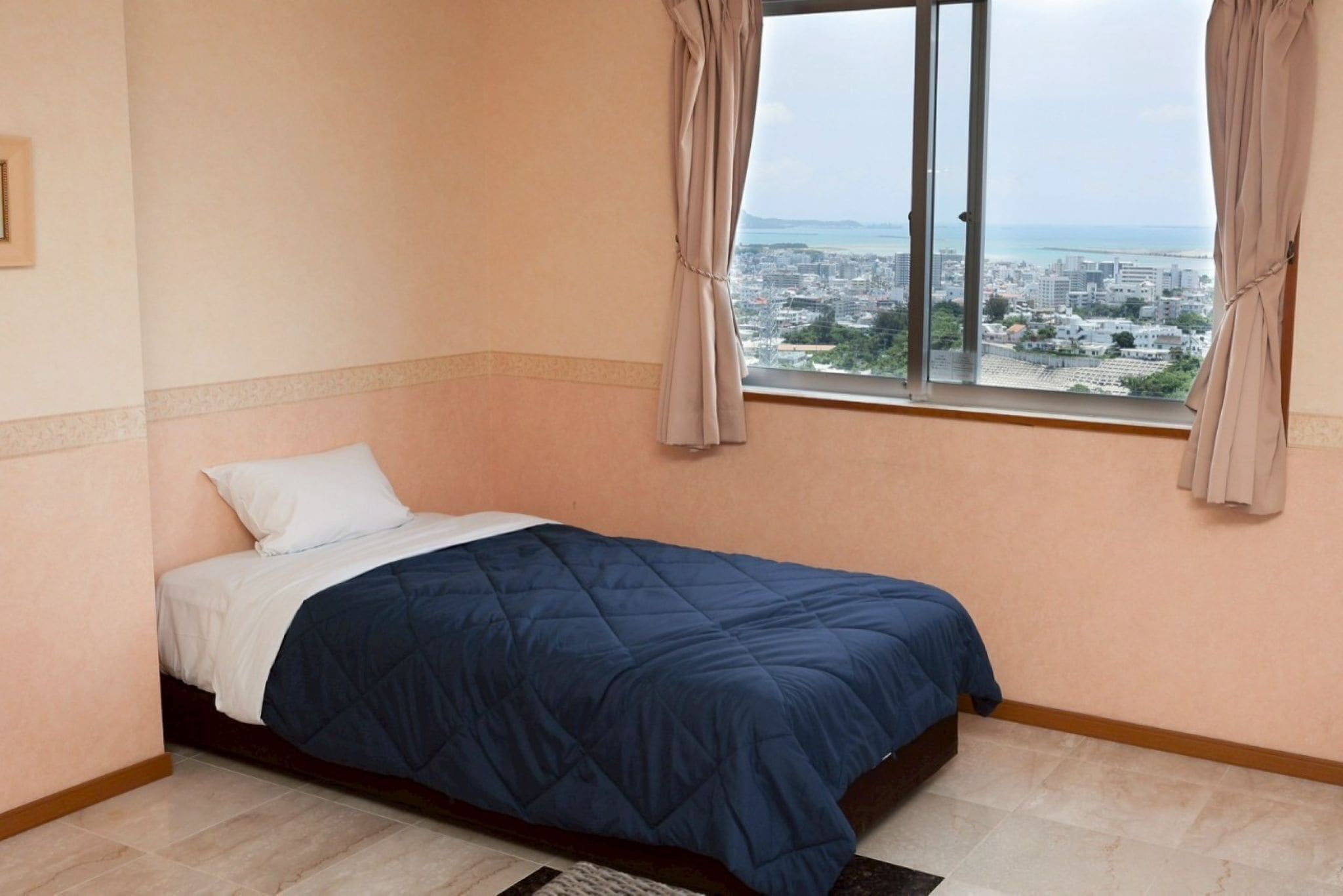 Ein Schlafzimmer mit einem Bett, einem Fenster mit Blick auf eine Stadtlandschaft und einem Vorhang.