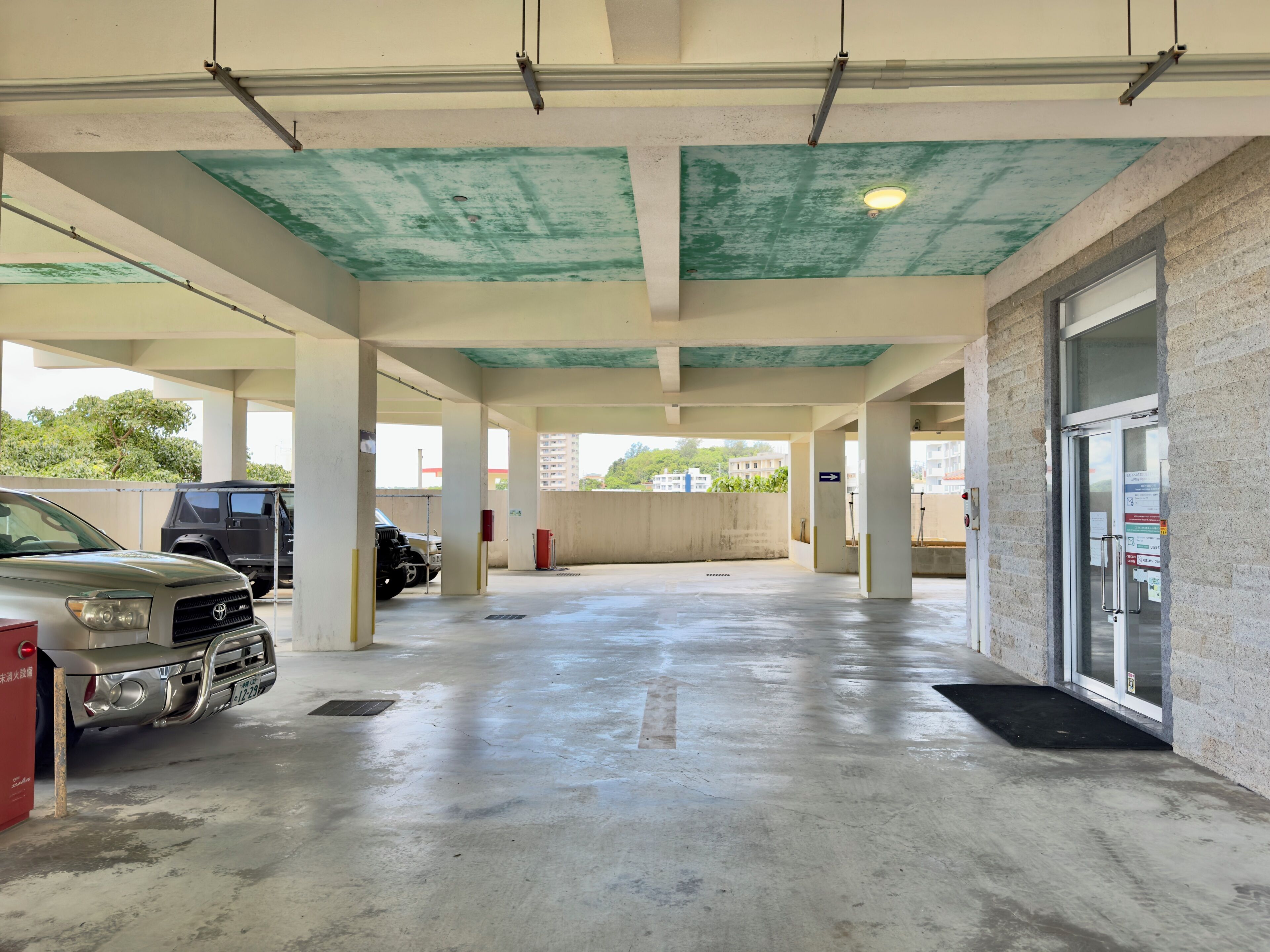 Un parking avec des planchers et des piliers en béton, quelques véhicules et une porte dotée d’un panneau de verre.