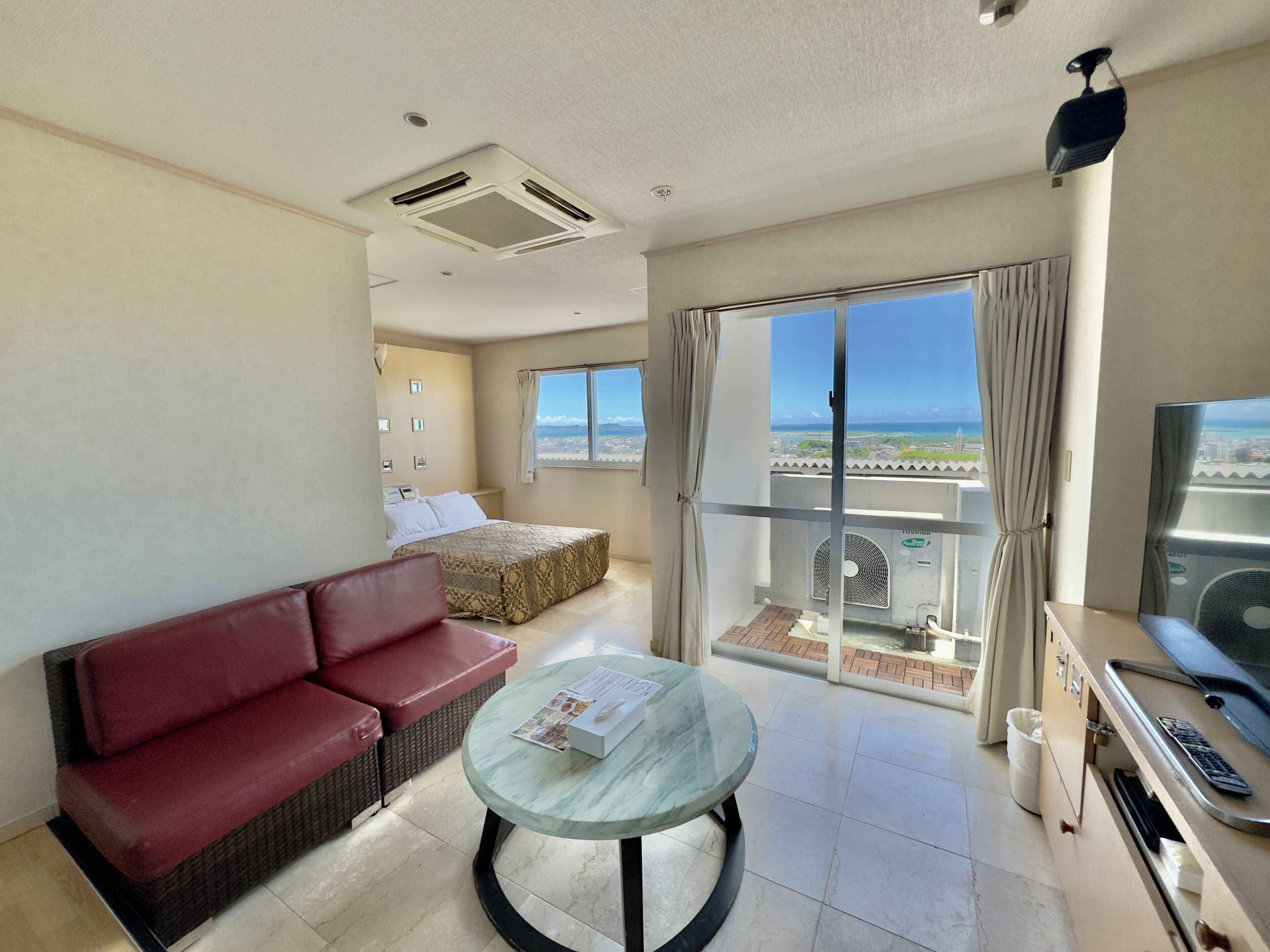 Een hotelkamer met balkon, een bed, een rode bank, een glazen tafel en een televisie.