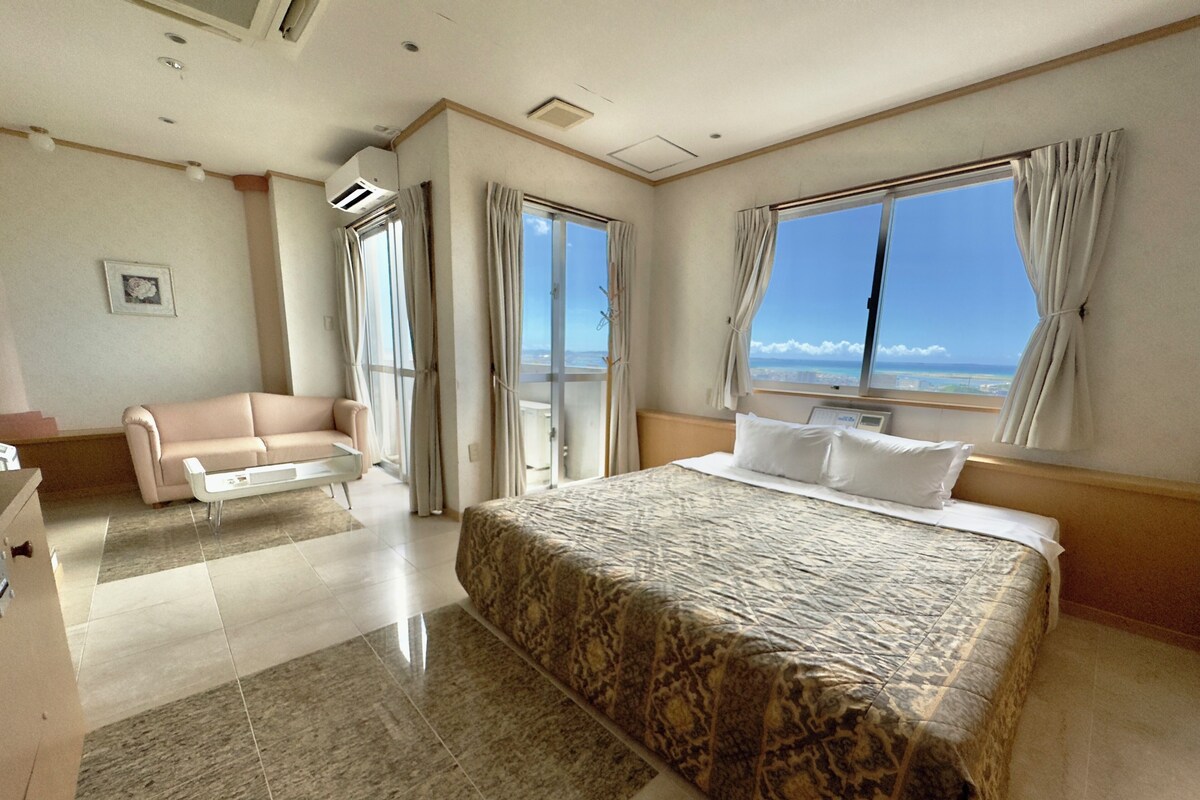 A hotel room with a large bed, a sofa, a desk, and a view of the ocean.
