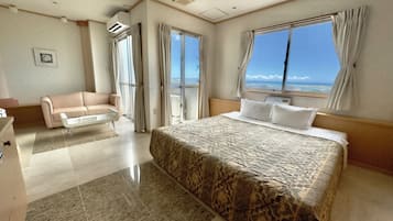 A hotel room with a large bed, a sofa, a desk, and a view of the ocean.