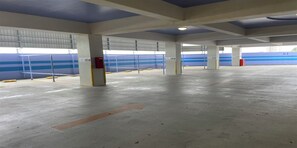 A spacious parking garage with concrete floors and columns, metal railings, and blue walls. - HOTEL PACIFIC VIEW (Okinawa)