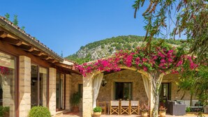 A stone building with a covered patio, outdoor seating, and a lush garden. - Villa Can Brullet by SunVillas Mallorca (Pollença)