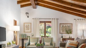 A living room with a wooden ceiling, striped sofas, a coffee table with decorative items, and a television on a wooden cabinet. - Villa Can Brullet by SunVillas Mallorca (Pollença)