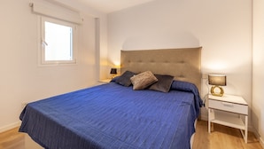 A bedroom with a large bed, two bedside tables, a window, and a wall-mounted lamp. - Apartment Faroles 1 By SunVillas Mallorca (Puerto Pollença)