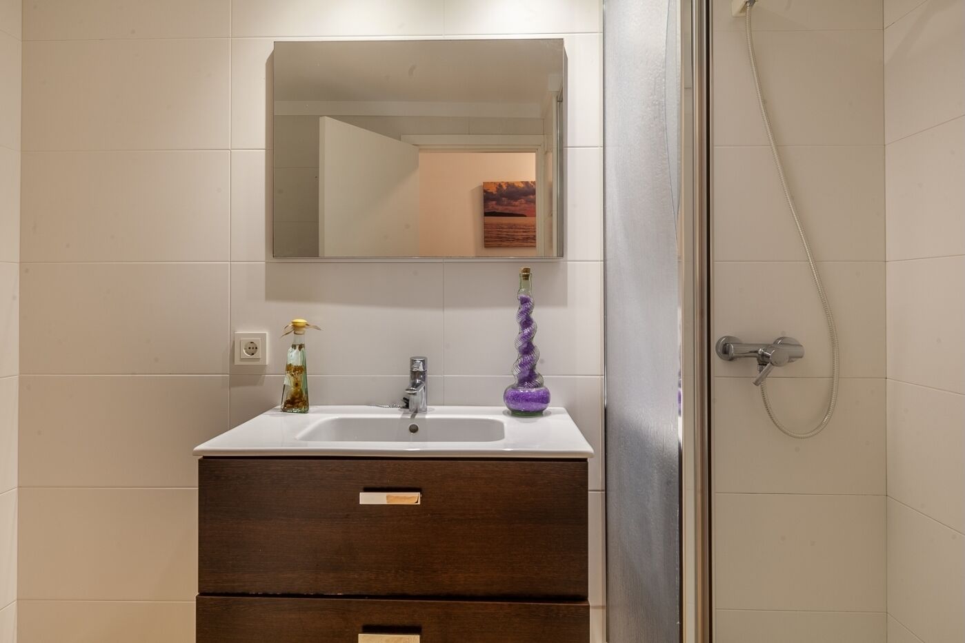 A bathroom with a white sink, a mirror, a purple vase, and a shower.