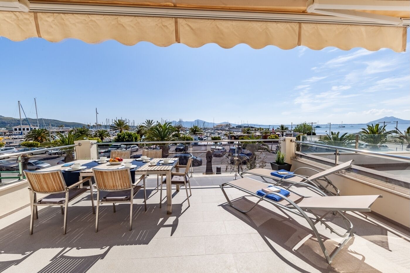 A terrace with tables and chairs, overlooking a marina with boats and a distant mountain.