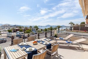 An outdoor dining area with tables set for two, overlooking a marina with boats and a clear sky. - Apartment Faroles 1 By SunVillas Mallorca (Puerto Pollença)