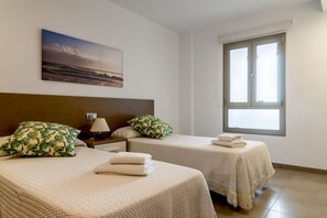 Une chambre d’hôtel avec deux lits, une table de chevet avec une lampe, un tableau au mur et une grande fenêtre.