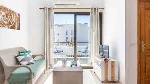 A modern living room with a sofa, a coffee table, a TV, and a balcony with a view of buildings. - Apartment Voltor 2 E By SunVillas Mallorca (Puerto Pollença)