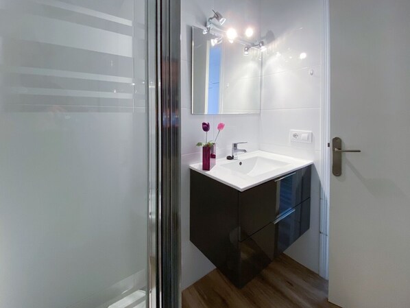 A modern bathroom with a glass shower enclosure, a white sink, and a dark vanity. - Apartment Gual 1 By SunVillas Mallorca (Puerto Pollença)