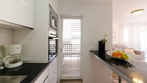 Een moderne keuken met een koffieapparaat, een inbouwoven en uitzicht op een balkon.