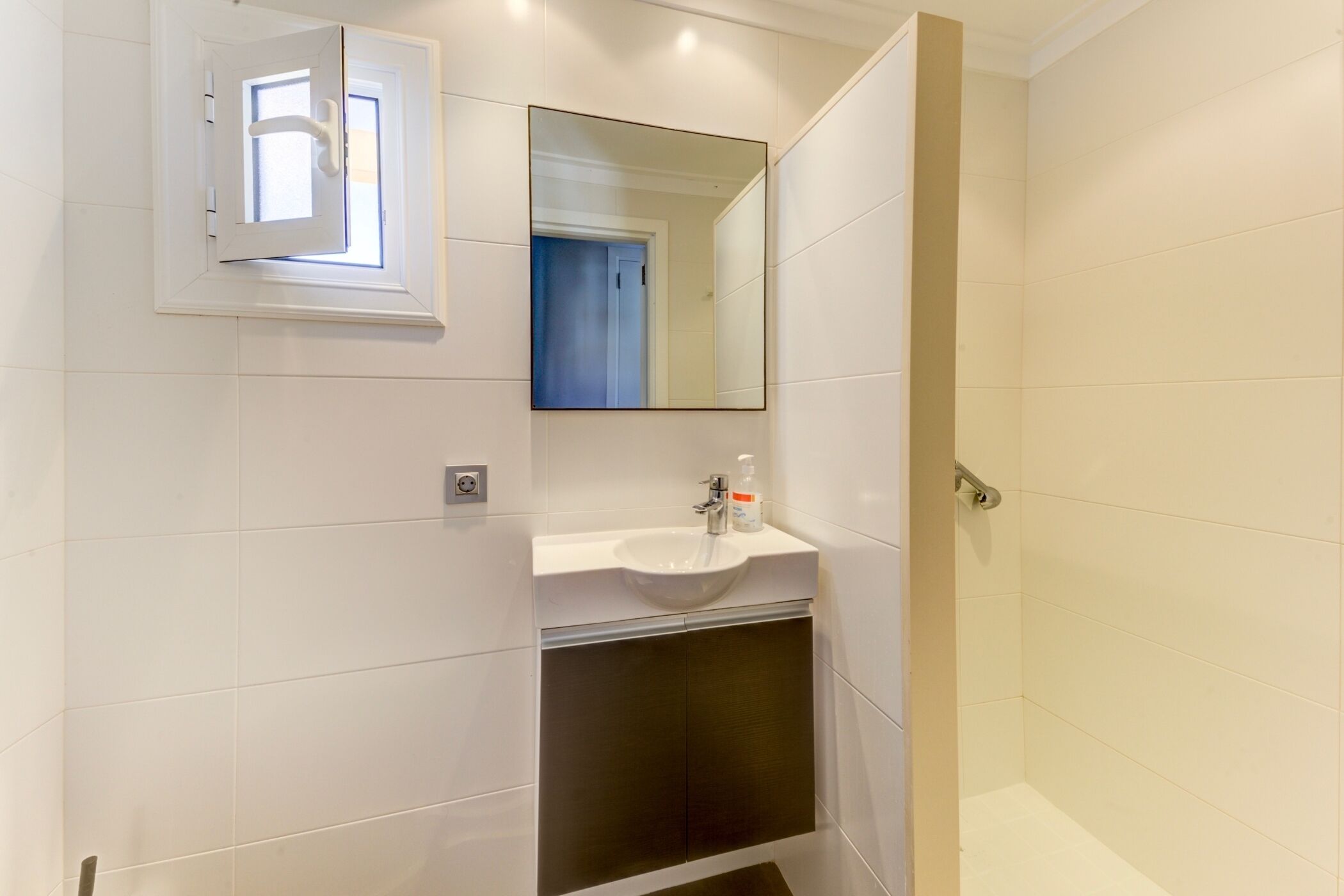 A bathroom with a white sink, mirror, and a shower area.