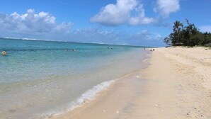 Uma praia com águas turquesa cristalinas, areal dourado e algumas pessoas a nadar.