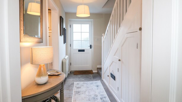 A hallway with a lamp, a mirror, a door, and a staircase. - Manor Barn Cottage (Bakewell)