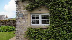 A stone cottage with a sign reading "Manor Barn Cottage," a window, and a stone wall. - Manor Barn Cottage (Bakewell)