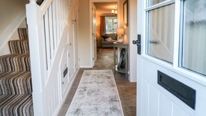 A hallway with a staircase, a rug, a door with frosted glass, and a sofa in the background. - Manor Barn Cottage (Bakewell)