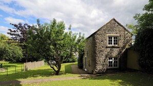 A stone building with a gabled roof, surrounded by a well-maintained lawn and trees. - Manor Barn Cottage (Bakewell)
