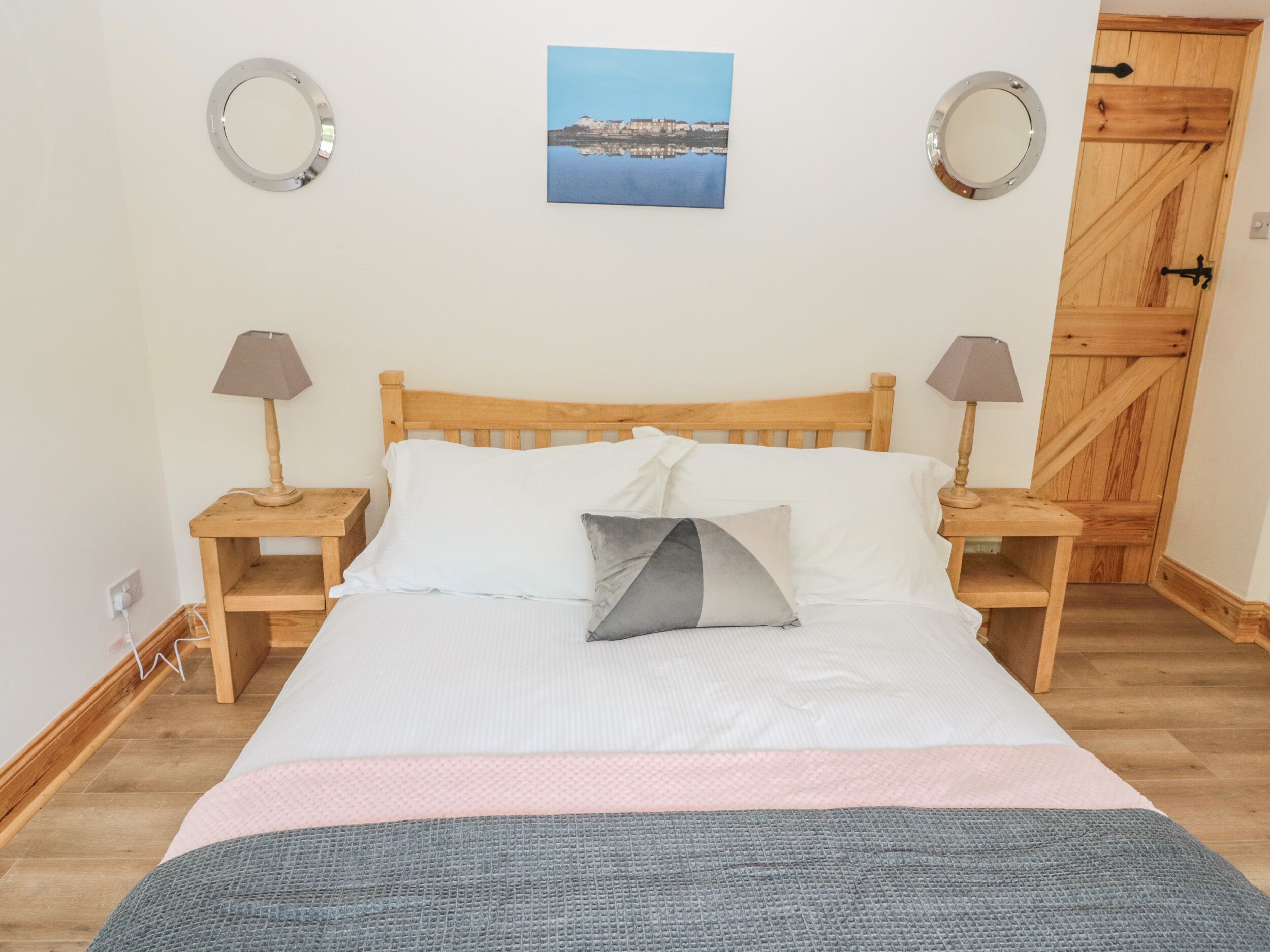 Ein Bett mit Holz Kopfteil, zwei Nachttische mit Lampen, ein Bild an der Wand und eine Holztür.