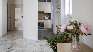 A modern kitchen with white cabinets, a wooden countertop, and a stainless steel oven. There is a vase with flowers on a table in the foreground. - Italianway Easy - Sirte 6 (Milan)
