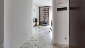A hallway leading to a living room with a marble floor, a bookshelf, a sofa, and a television. - Italianway Easy - Sirte 6 (Milan)
