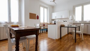 Une cuisine moderne avec des meubles blancs, une table à manger en bois et un petit îlot central doté d’un évier.