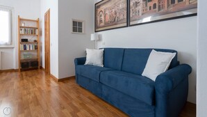 Une pièce avec un canapé bleu, un plancher en bois, une bibliothèque et un tableau encadré au mur.