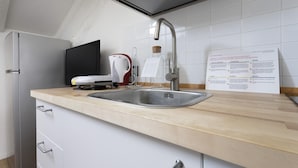 Eine moderne Küche mit Spüle aus Edelstahl, Wasserkocher und Halterung dafür. An der Wand befindet sich ein Schild zur Mülltrennung.
