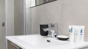 Ein modernes Badezimmer mit einem weißen Waschbecken, einem schwarzen Seifenspender und drei Kosmetiktaschen auf der Ablagefläche.
