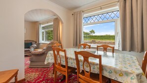 A dining area with a table set for four, a sofa, and a window with a view of the countryside. - Trefelyn Cottage in Saundersfoot (Saundersfoot)