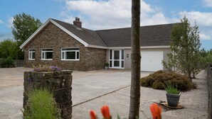 A two-story stone house with a garage, a driveway, and a landscaped garden with a stone planter and flowering plants. - Trefelyn Cottage in Saundersfoot (Saundersfoot)