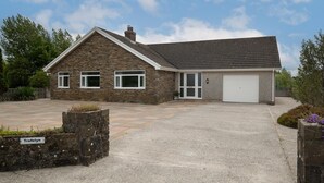 A stone house with a garage, a driveway, and a stone wall with a sign. - Trefelyn Cottage in Saundersfoot (Saundersfoot)