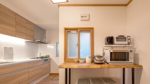 A modern kitchen with wooden cabinets, a built-in oven, a microwave, and a coffee maker. There are three trash bins under a wooden table. - Toya Cliff House (Toyako)
