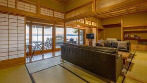 A traditional Japanese room with tatami flooring, a sofa, a television, and a view of the sea. - Toya Cliff House (Toyako)