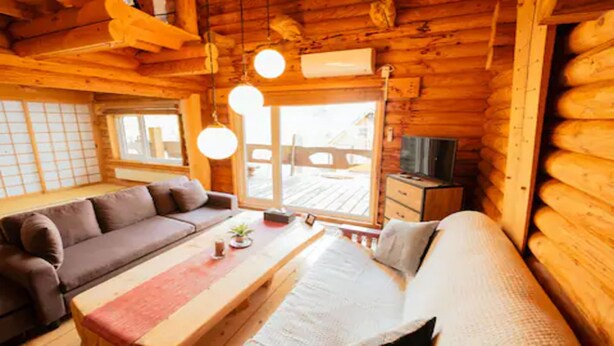 Ein rustikales Blockhaus-Interieur mit einer Couch, einem kleinen Tisch und einem Fernseher auf einem Holzkabinett.