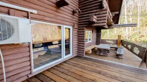 Eine Blockhütte mit einer Holzterrasse, großen Fenstern und einem kleinen Sitzbereich im Freien.