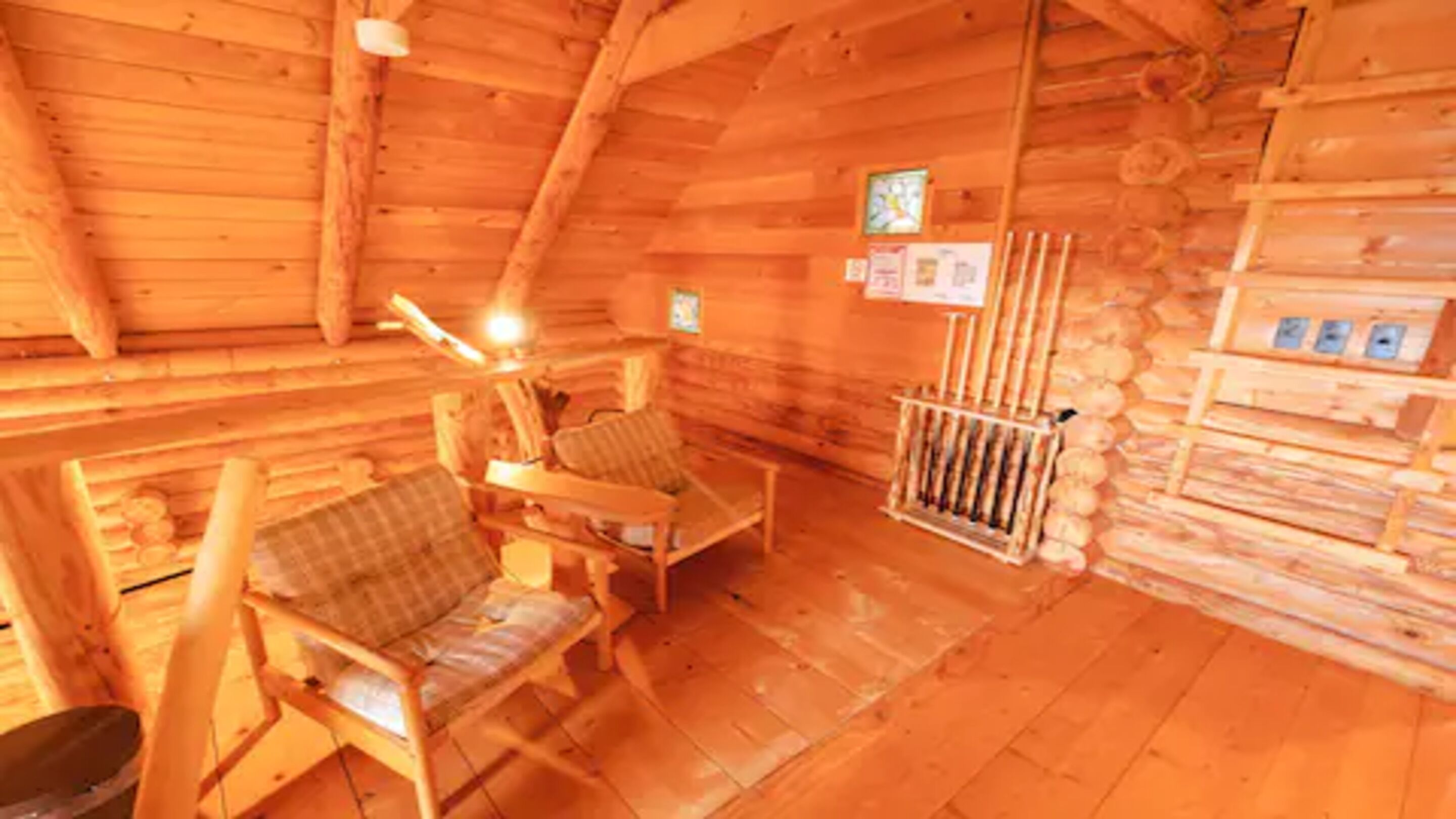 A cozy log cabin interior with wooden walls, a fireplace, two wooden chairs, and a small table.