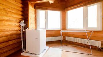 A log cabin room with a water heater, radiator, and a window with a metal frame.
