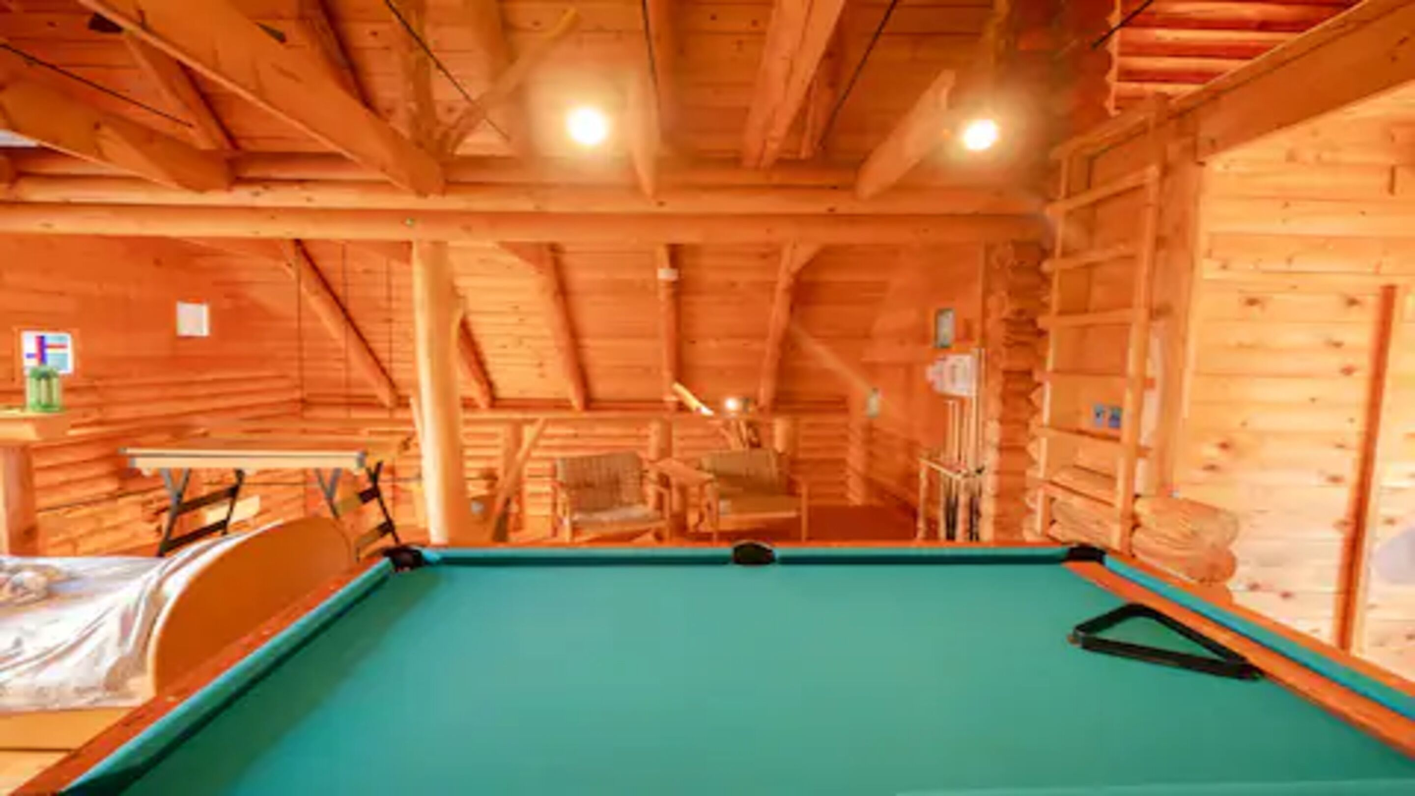 Een pooltafel in een houten blokhut met een hoge nok en houten wanden.