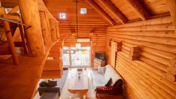 A log cabin interior with a loft area, a sofa, a dining table, and a television.