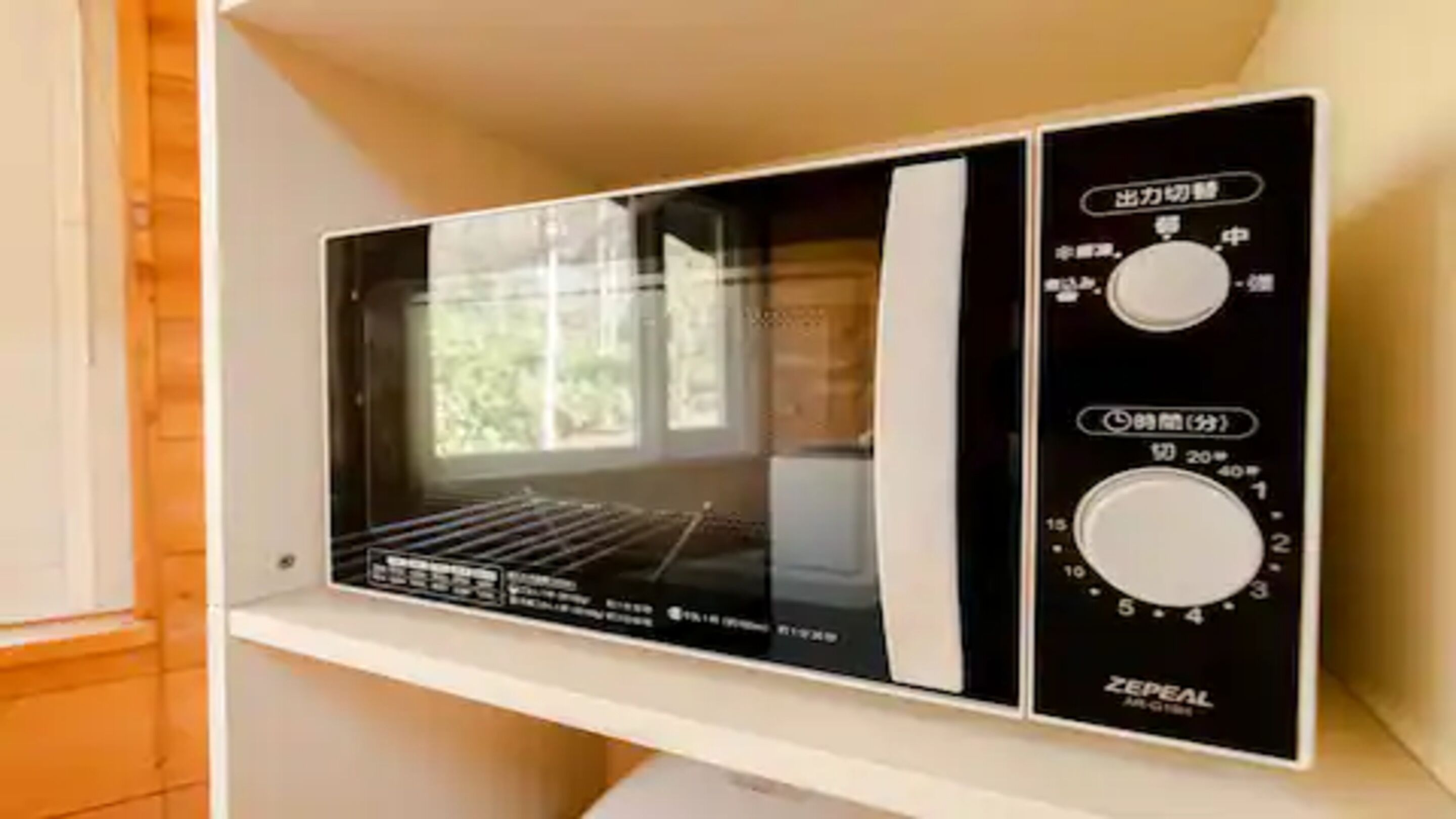 Un four à micro-ondes doté de deux boutons de commande et d’un écran numérique, placé sur une étagère blanche dans une cuisine.