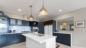 Uma cozinha moderna com armários azul escuro, uma ilha branca, eletrodomésticos de aço inoxidável e iluminação pendente.