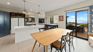 Uma cozinha moderna com uma ilha central, área de refeições com cadeiras e vista para um pátio exterior através de uma porta de vidro.