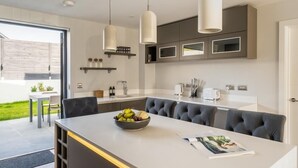 Een moderne keuken met een centraal eiland, hangende verlichting en inbouwmeubels.