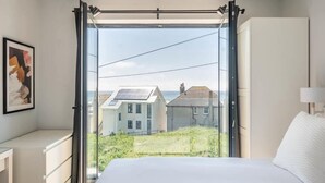Ein Schlafzimmer mit großem Fenster, einem Bett, einer Kommode und einem Bild an der Wand.