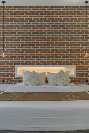A bedroom with a brick wall, a white bed, two pillows with star patterns, and two hanging light bulbs.