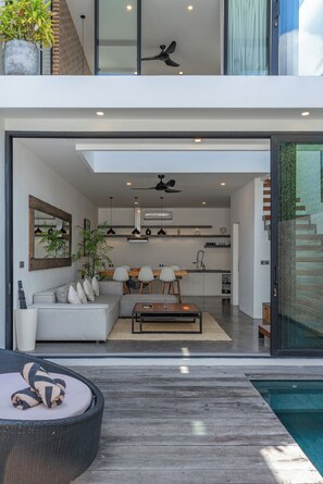 A modern interior with a dining area, kitchen, and a poolside seating area.